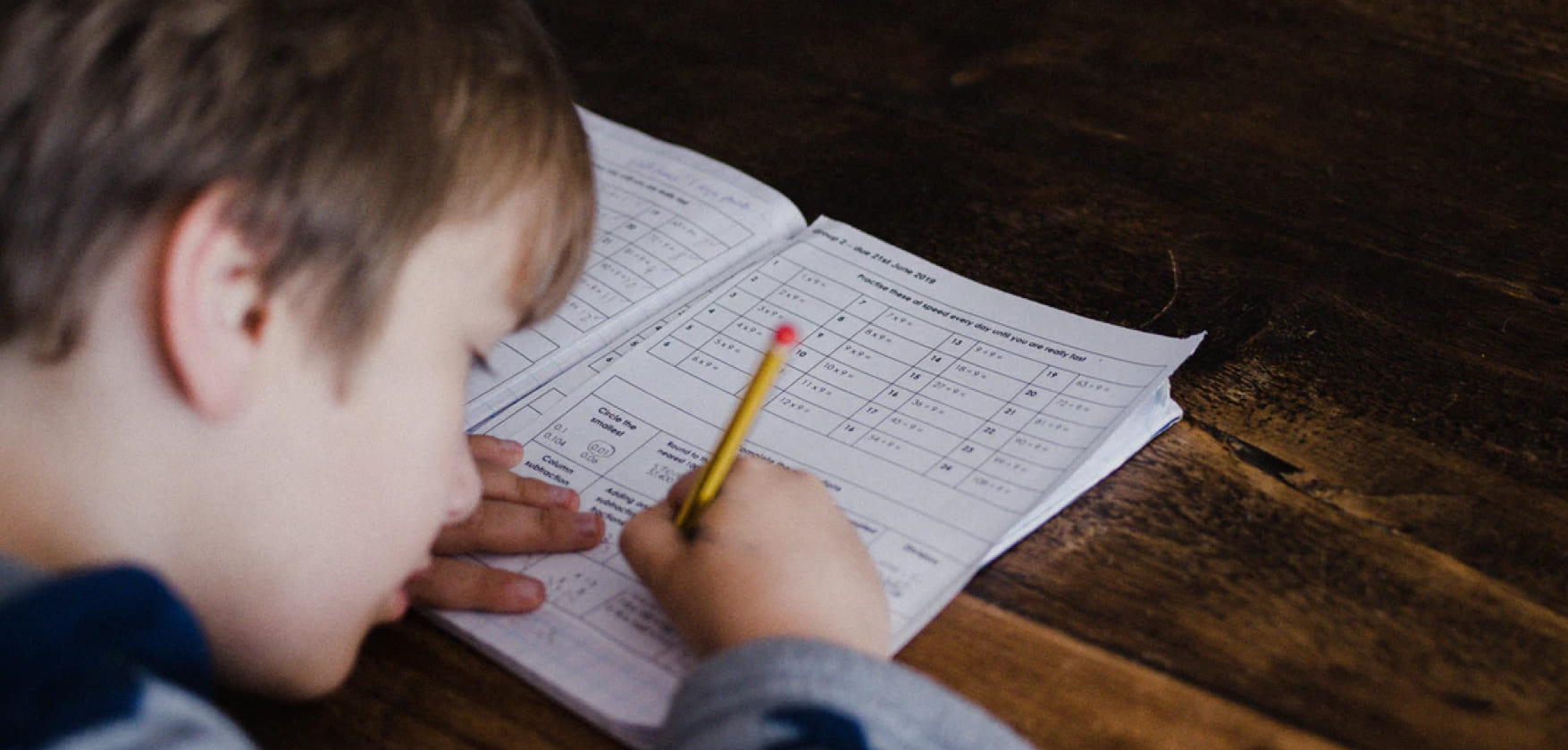 写真：ペンを持った少年が机上でノートに何か書き込んでいる様子